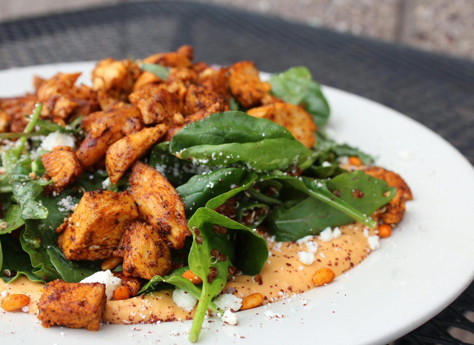 Delicious chicken salad with spinach, feta cheese, and creamy sauce on a white plate.